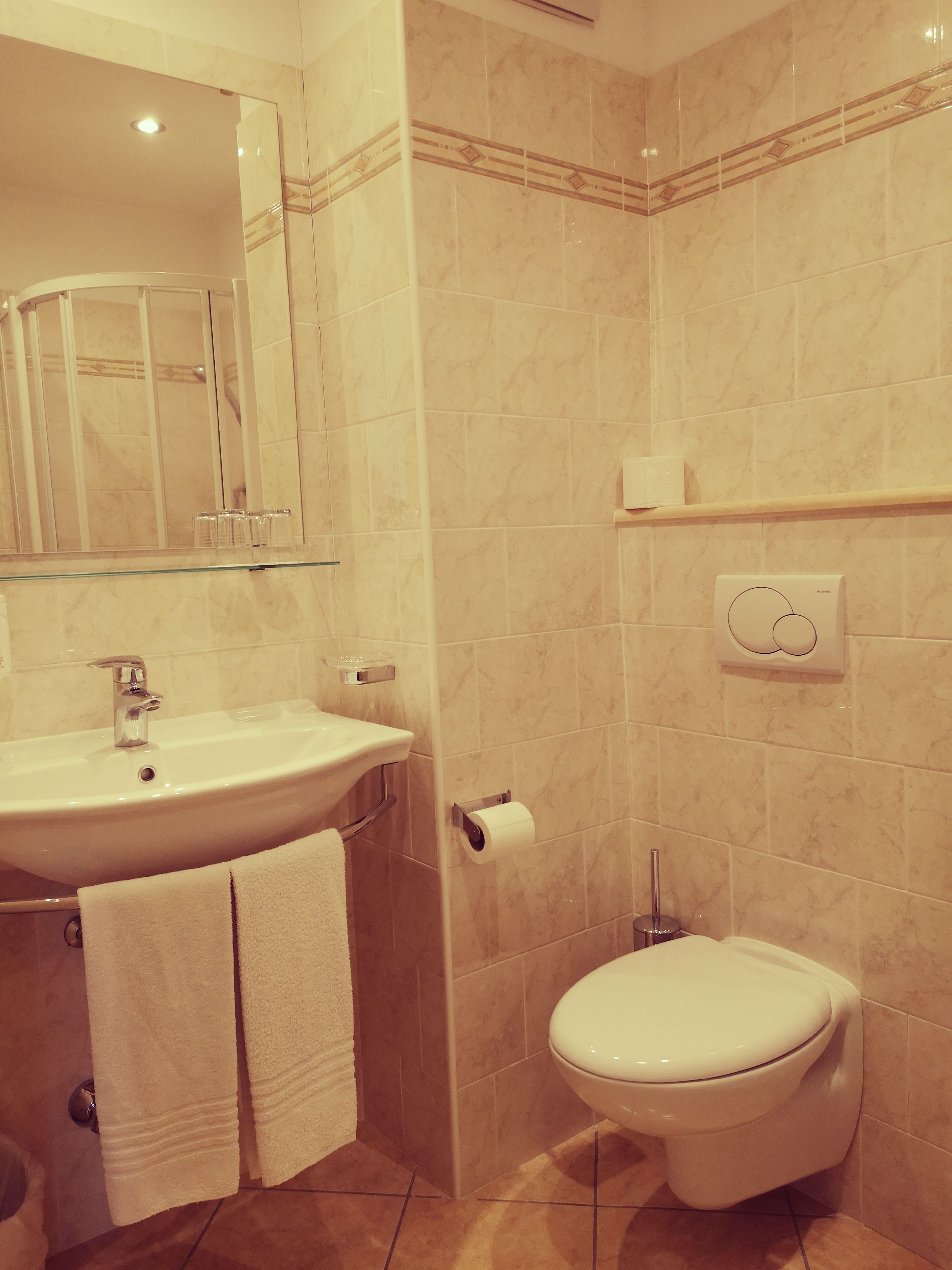 A bathroom with a sink, mirror, towel rack, toilet, and a towel dispenser.
