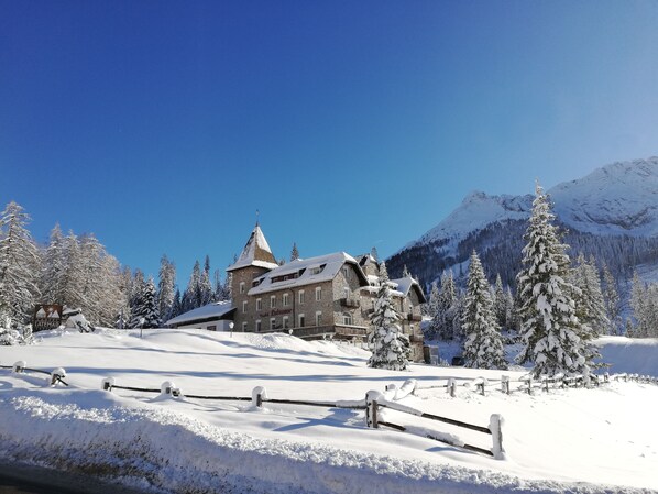 Ein historisches Gebäude mit einem markanten Turm, umgeben von schneebedeckten Bäumen und Bergen.