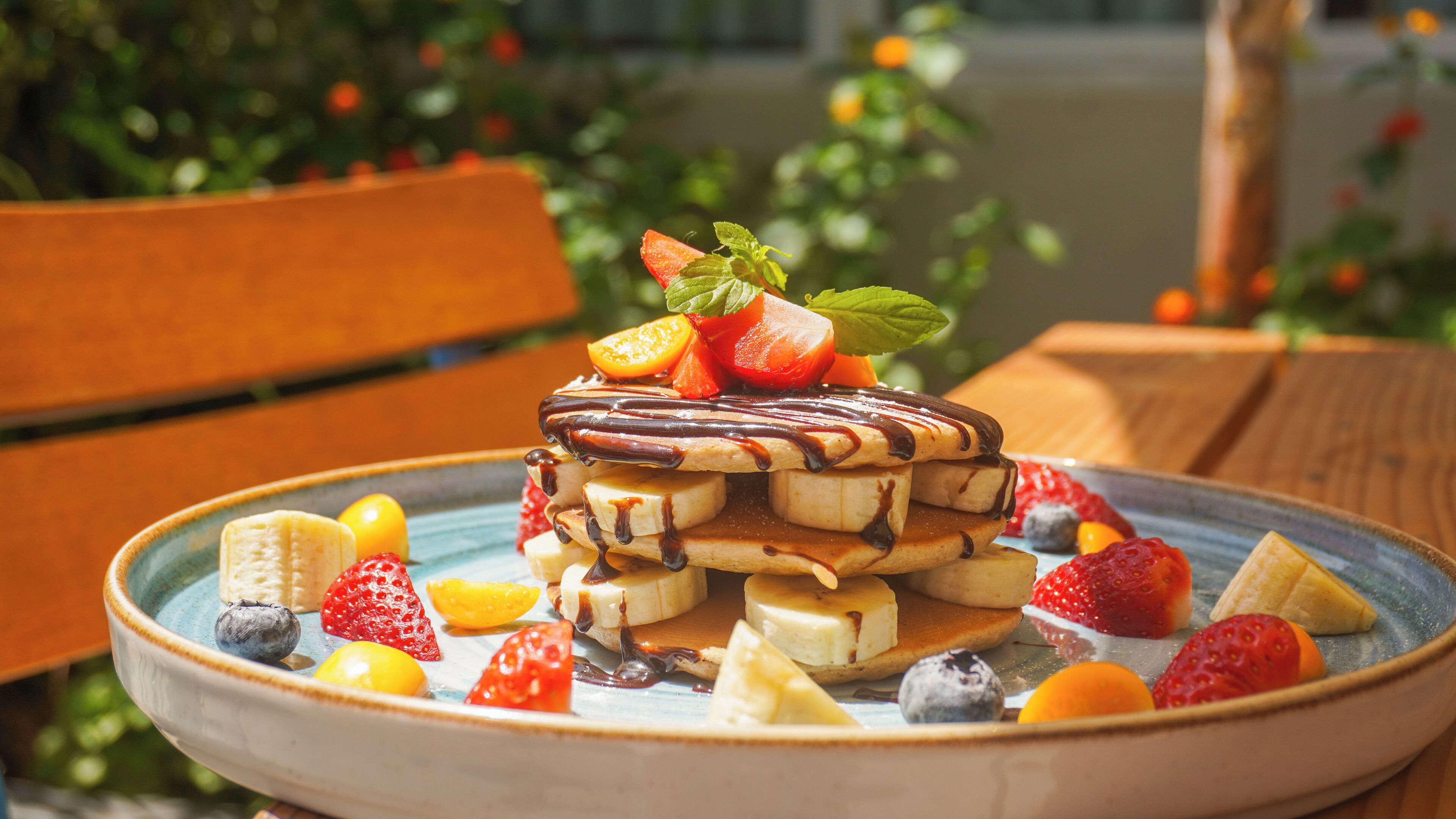 A plate of pancakes with fruit and chocolate sauce.