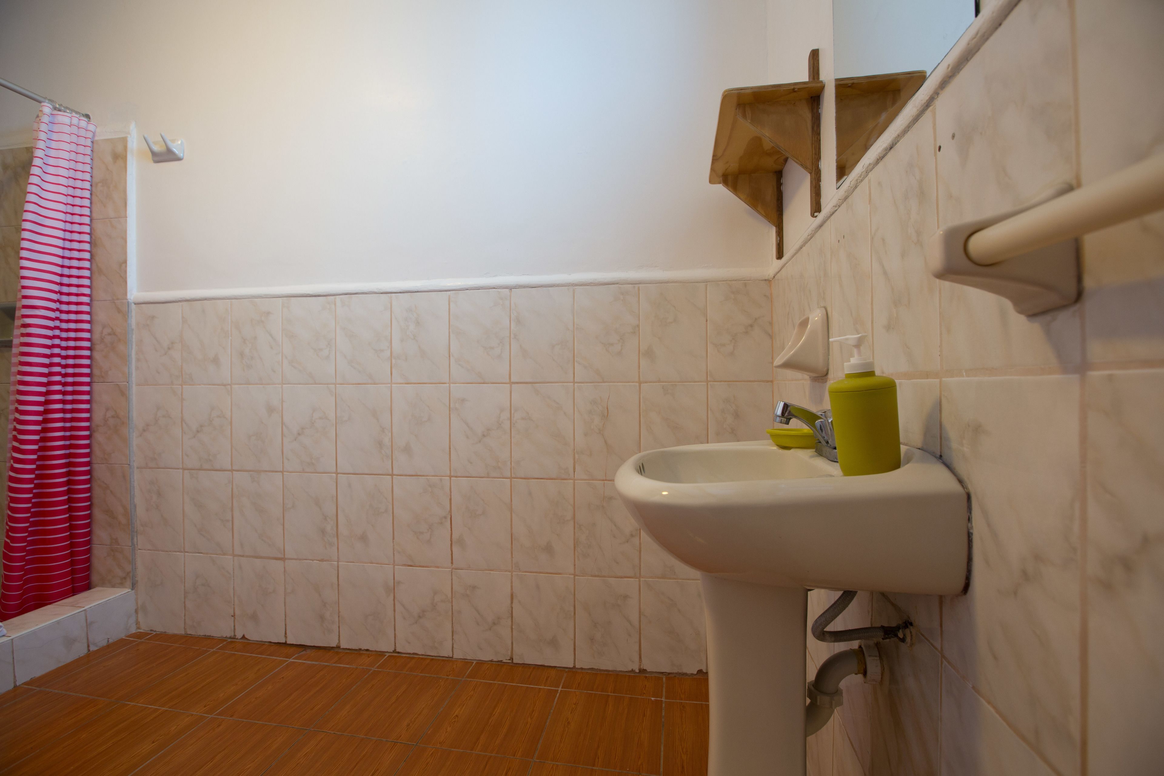 Un baño con un lavamanos blanco, una botella amarilla y una cortina de ducha a rayas rojas y blancas.