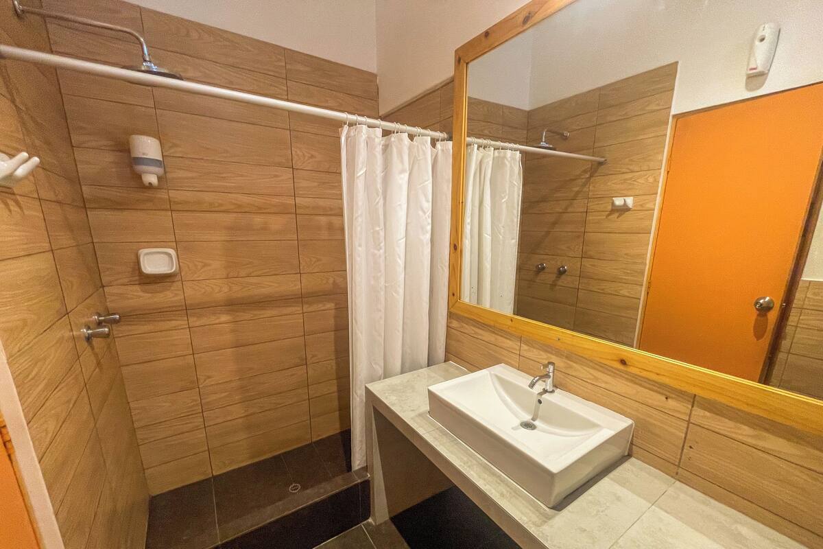 A bathroom with a wooden shower enclosure, a white sink, and a mirror with a wooden frame.