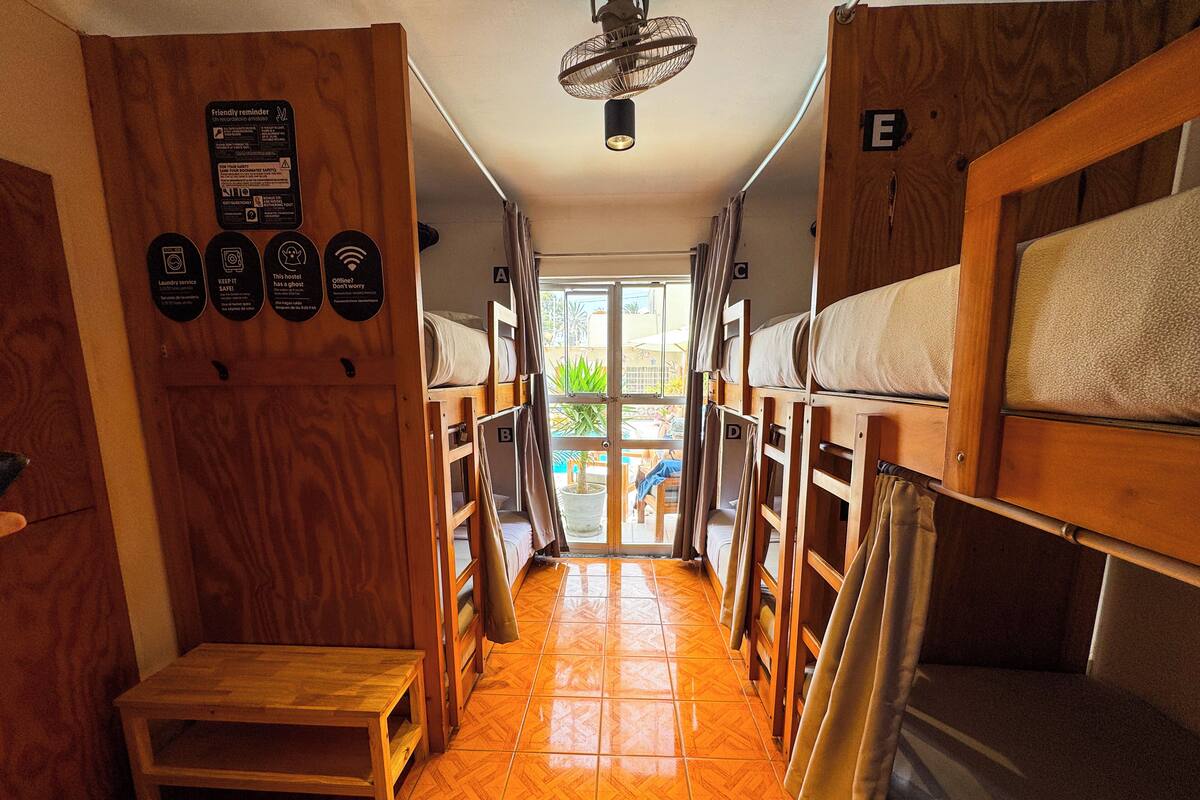 A corridor with bunk beds, a wooden bench, and a door leading outside.