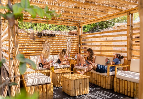 A bamboo pergola with seating areas, including cushioned chairs and benches.