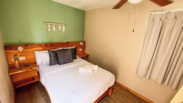 Una cama bien hecha con sábanas blancas, cabecera de madera y ventilador de techo.