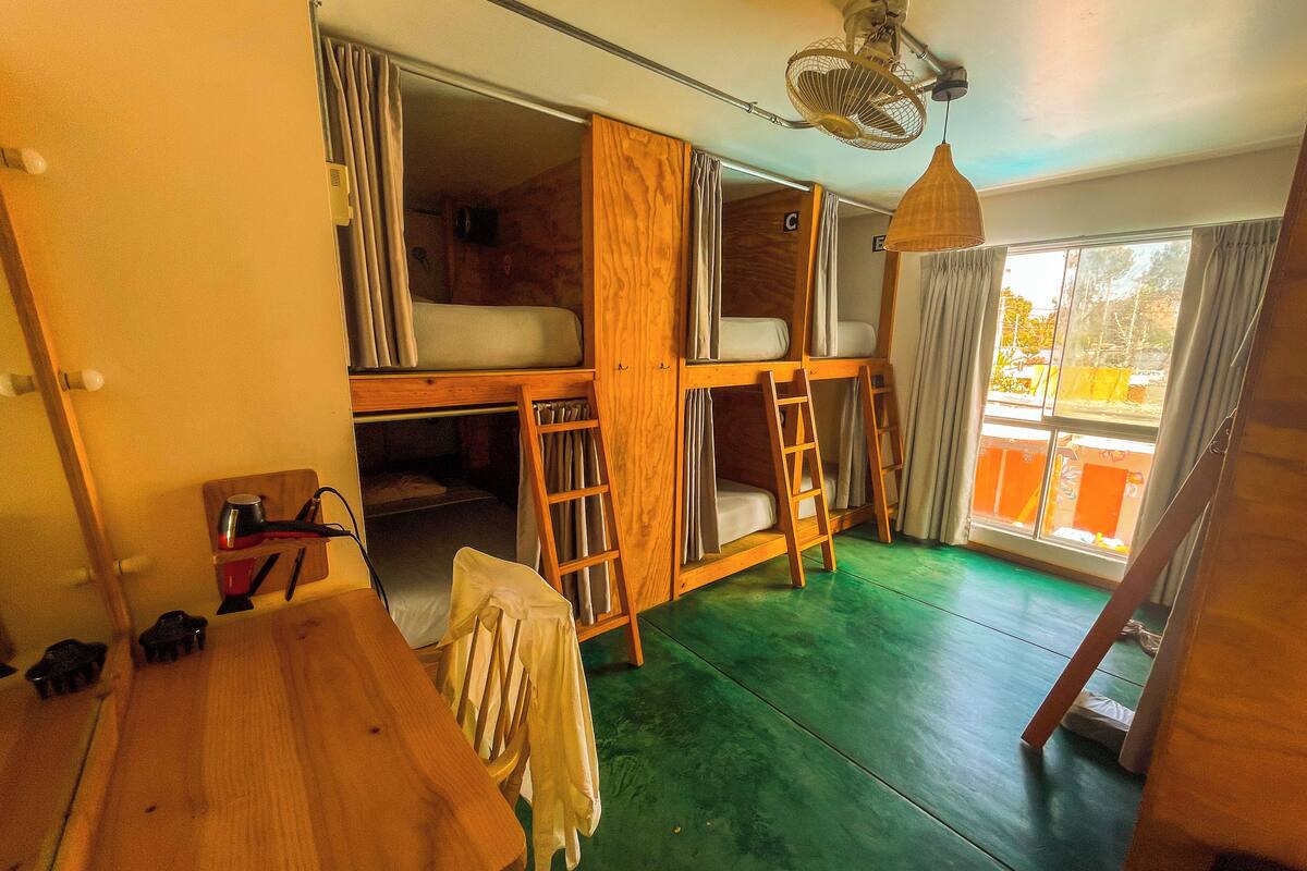 A room with bunk beds, a wooden table, a chair, a ceiling fan, and a window with curtains.