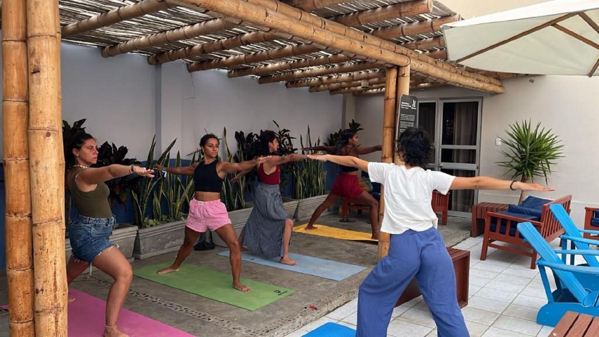 A group of people practicing yoga outdoors under a bamboo structure.
