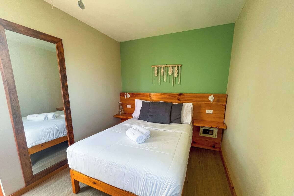 A neatly made bed with white linens and towels, a wooden headboard, and a bedside table with a lamp.
