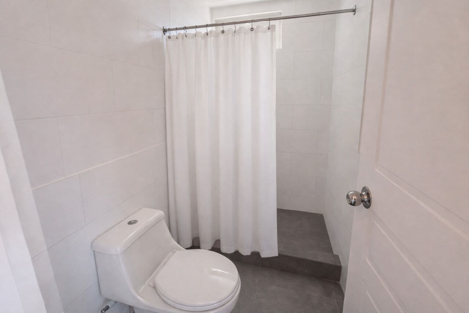 A small, clean bathroom with a toilet, a shower curtain, and tiled walls.