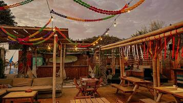 Un patio al aire libre con mobiliario de madera y luces colgantes.