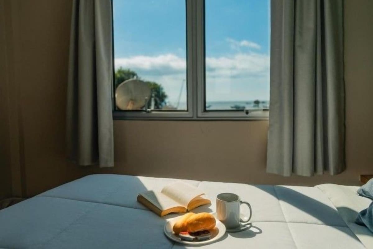 Un lit avec vue sur la mer, un livre, une banane et une tasse.