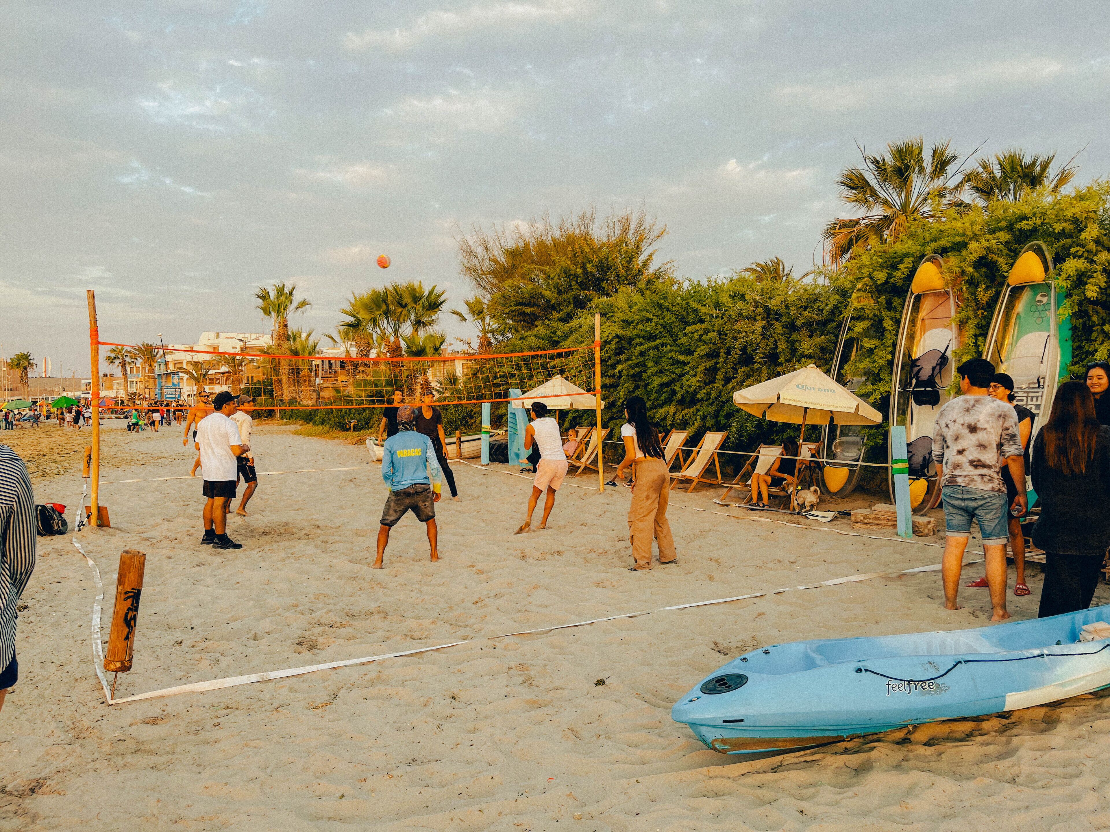 A beach volleyball court with players, beach chairs, and umbrellas.