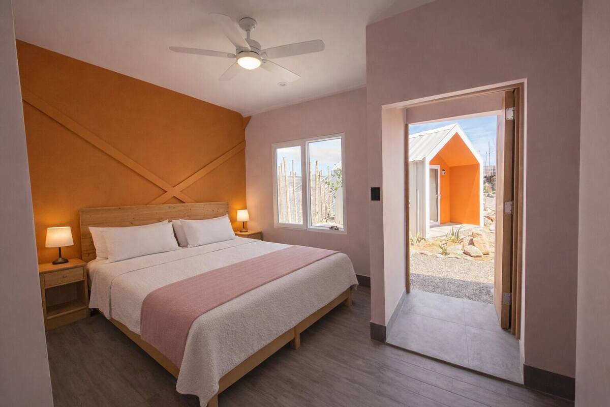 A bedroom with a bed, nightstands, a ceiling fan, and a view of the outside.