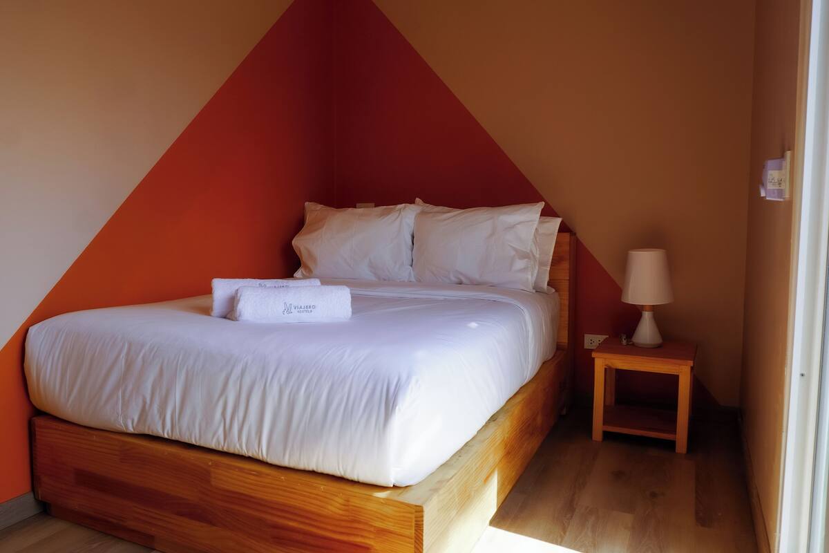 A neatly made bed with white linens and a towel, a wooden nightstand with a lamp, and a red and beige wall.