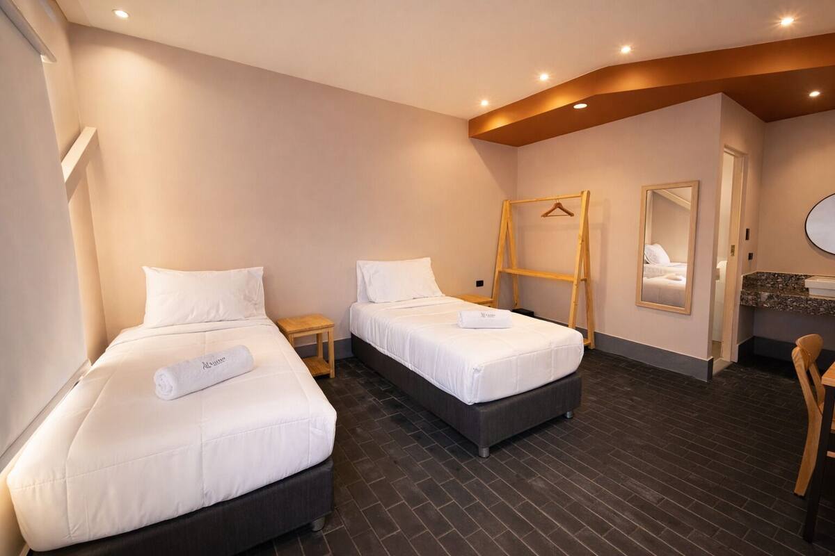 A hotel room with two beds, a wooden ladder, a mirror, and a small table.