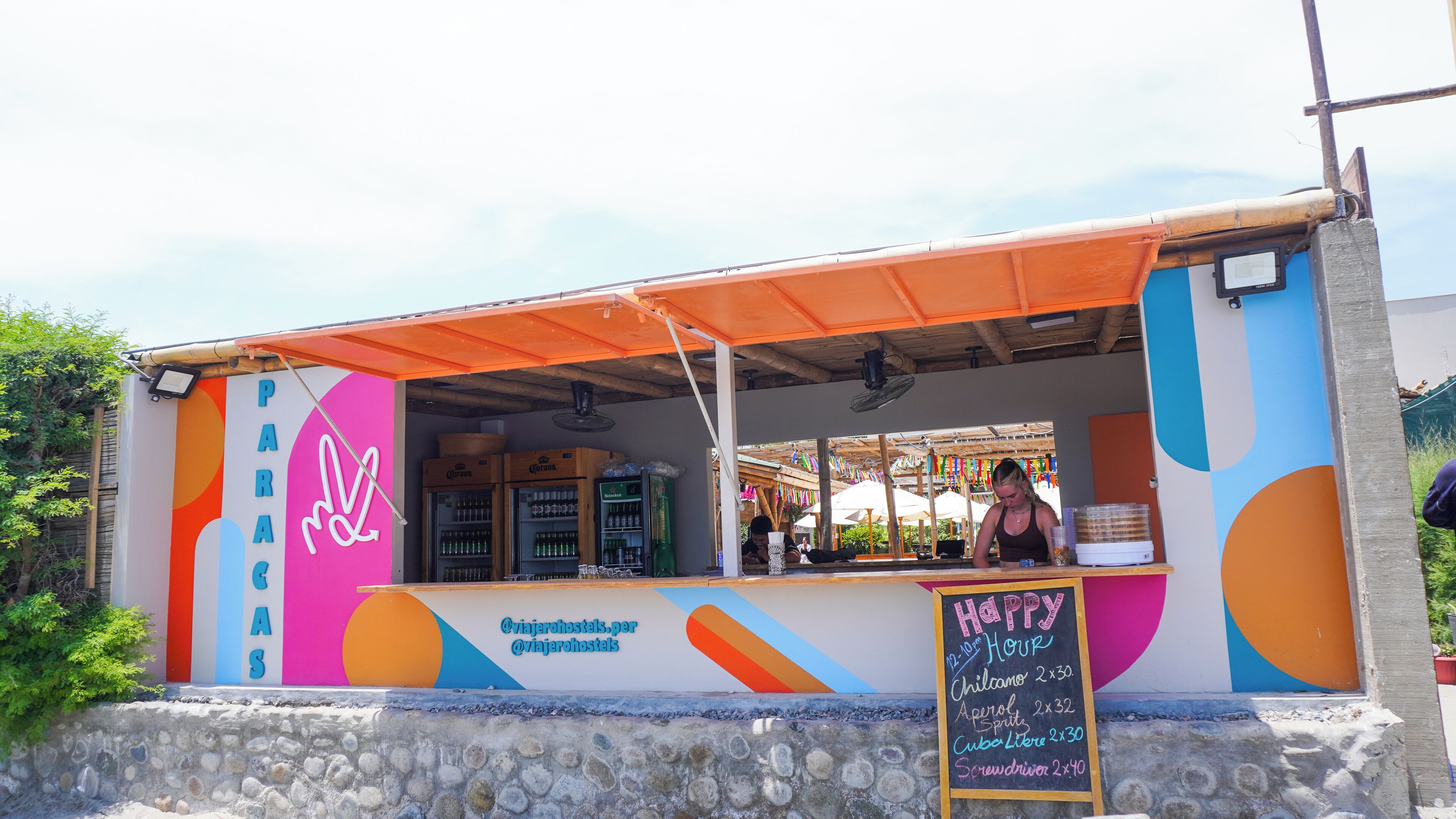 Un camión de comida colorido con un menú en una pizarra que enumera artículos como 'Chilcano' y 'Aperol Spritz'.