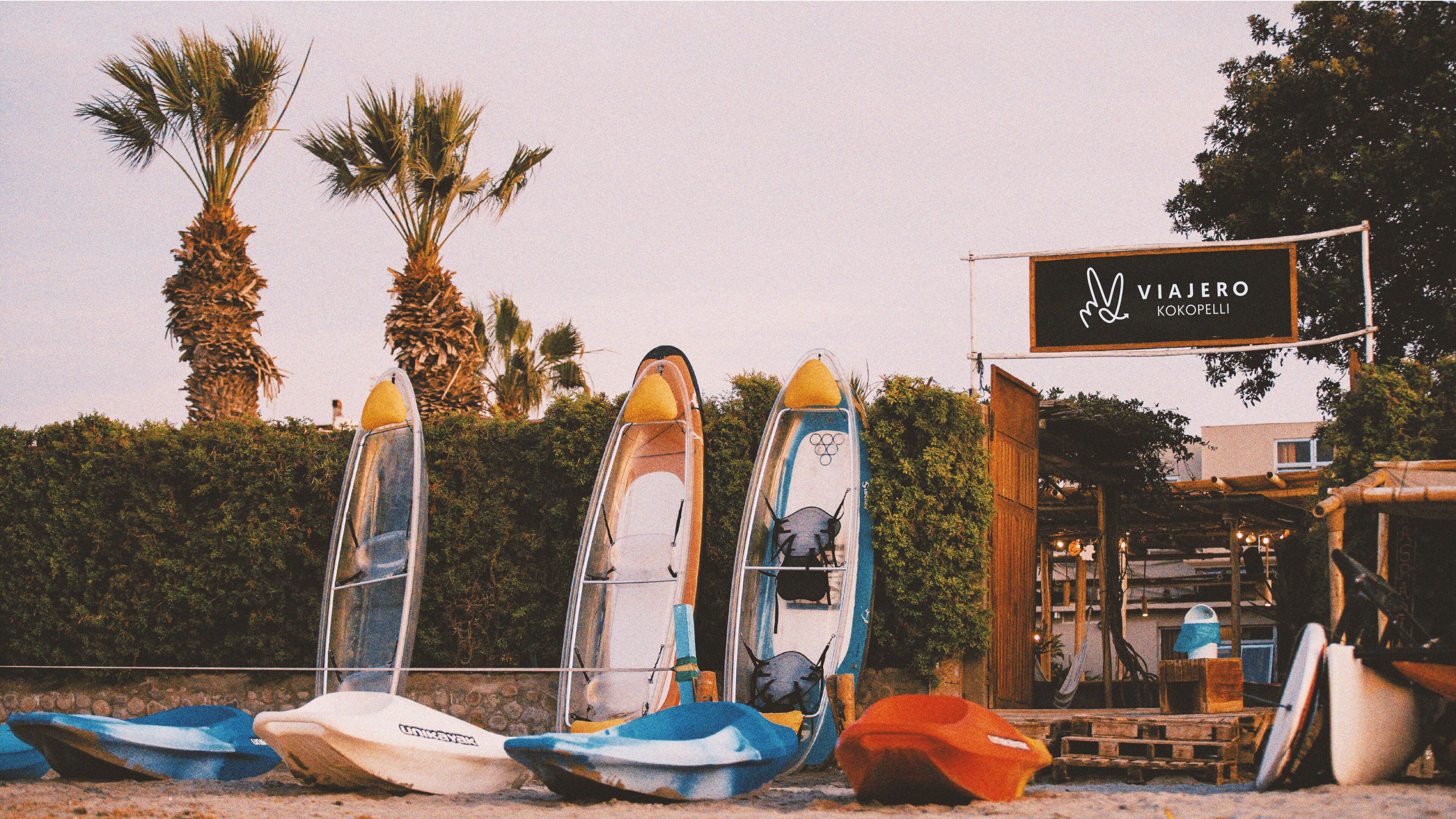 A beachside location with several kayaks lined up and a signboard for 'Vajero Kokopelli'.