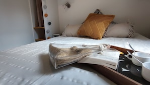A neatly made bed with a white duvet, a brown throw pillow, and a book with a straw bag beside it. There are two white cups and a spoon on a tray. - Camping de Santenay (Santenay)
