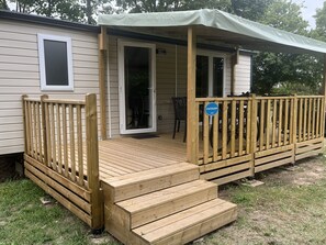 Uma casa móvel com um deck de madeira, um alpendre coberto e uma porta de correr.