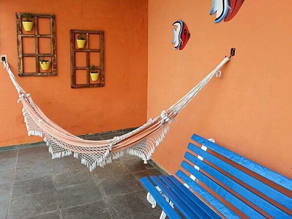 A hammock hanging between two windows, a blue bench, and a tiled floor. - Pousada Porto Paraíso (Guarujá)