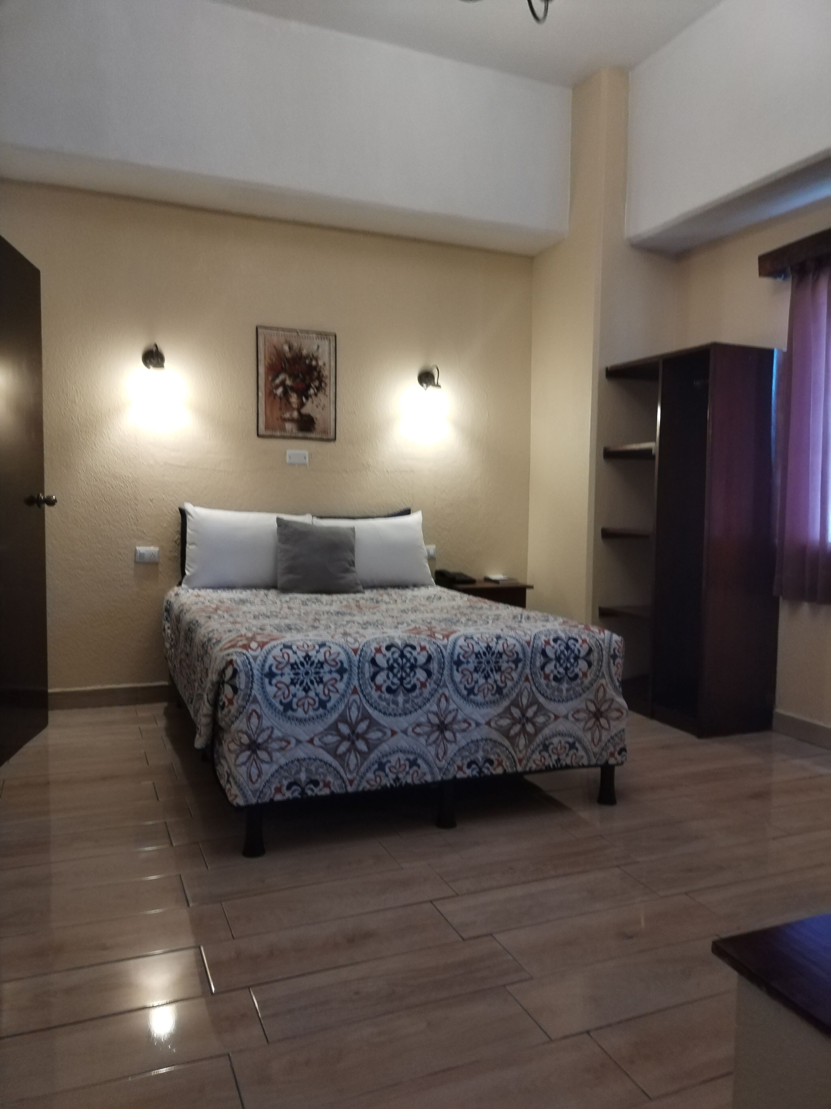 Un dormitorio con una cama, dos luces empotradas en la pared, una mesita de noche, un aparador y un cuadro en la pared.