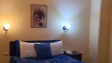 Een hotelkamer met een bed, twee bedlampen, een kroonluchter en een schilderij aan de muur.