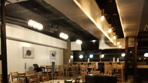 A restaurant with a long communal table surrounded by chairs, a bar area, and a small garden with plants.