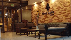A lobby with a brick wall, a sofa, two armchairs, a coffee table, and a potted plant.