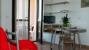 A modern living room with a red sofa, a dining table with four chairs, a TV, and a potted plant. - RTA Martin Pescatore (Grosseto)