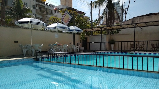 Una piscina con suelo de baldosas, rodeada de sillas de plástico blancas y sombrillas.