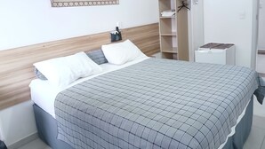 Una cama bien hecha con colcha a cuadros, cabecera de madera y un cuadro colgado en la pared.