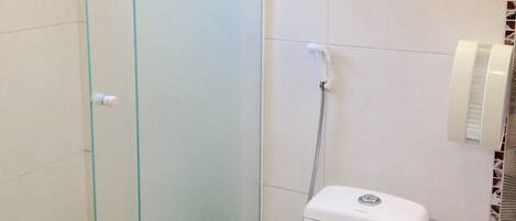 A bathroom with a glass shower enclosure, a toilet, and a towel rack with two towels.