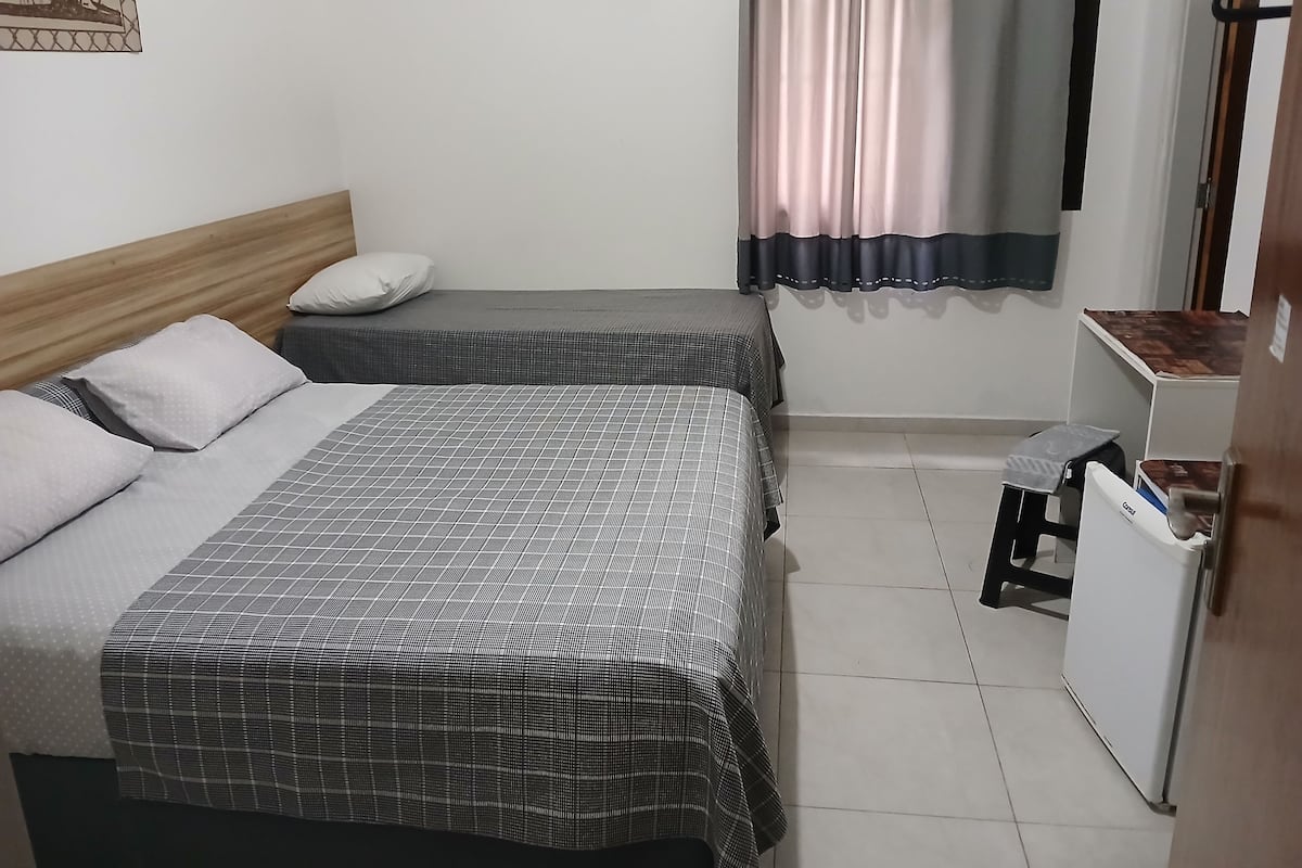 A bedroom with two beds, a small desk, and a refrigerator.
