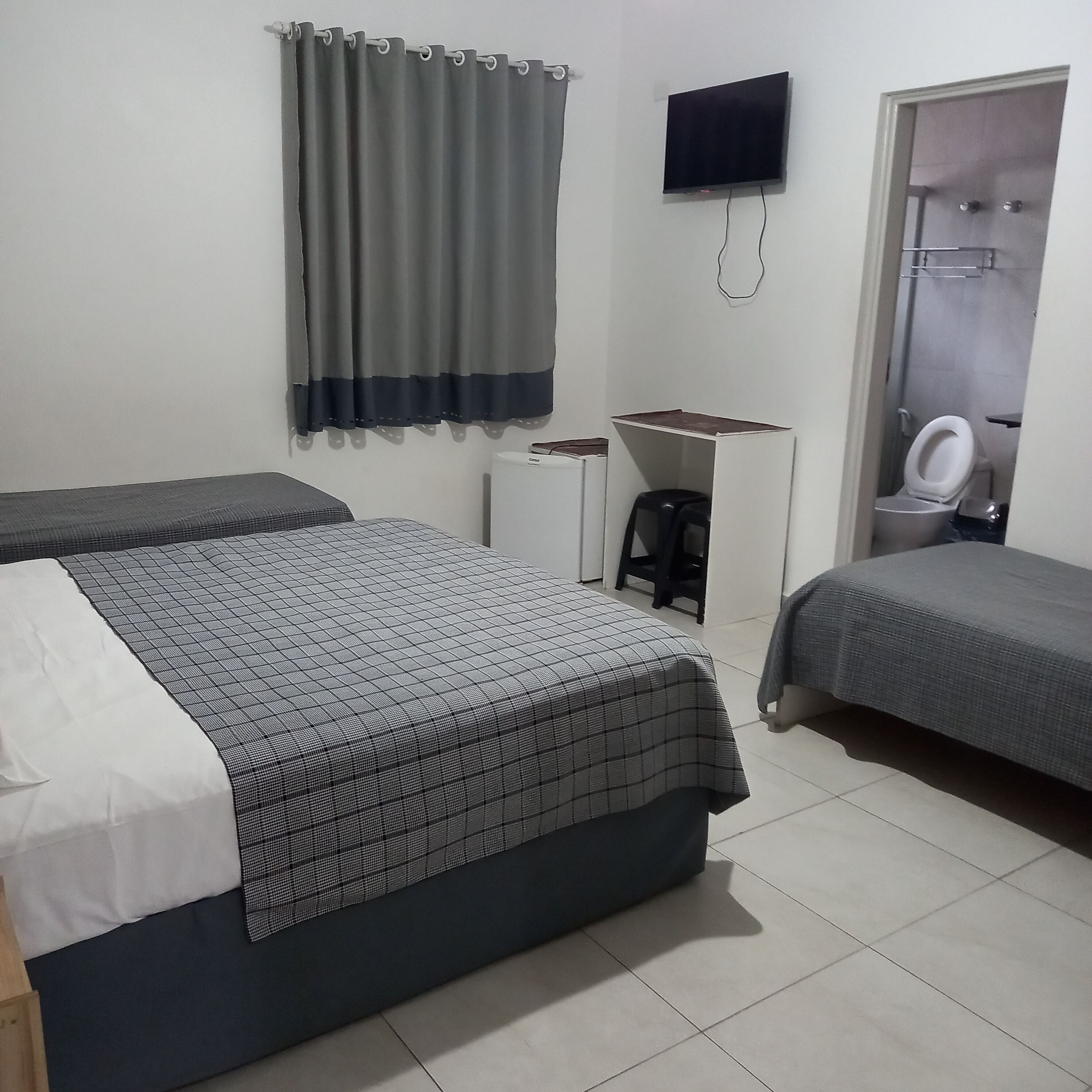A hotel room with two beds, a TV, a desk, and a toilet.
