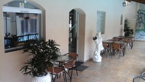 Un espacio de descanso al aire libre con mesas y sillas, una planta grande en maceta y una estatua.