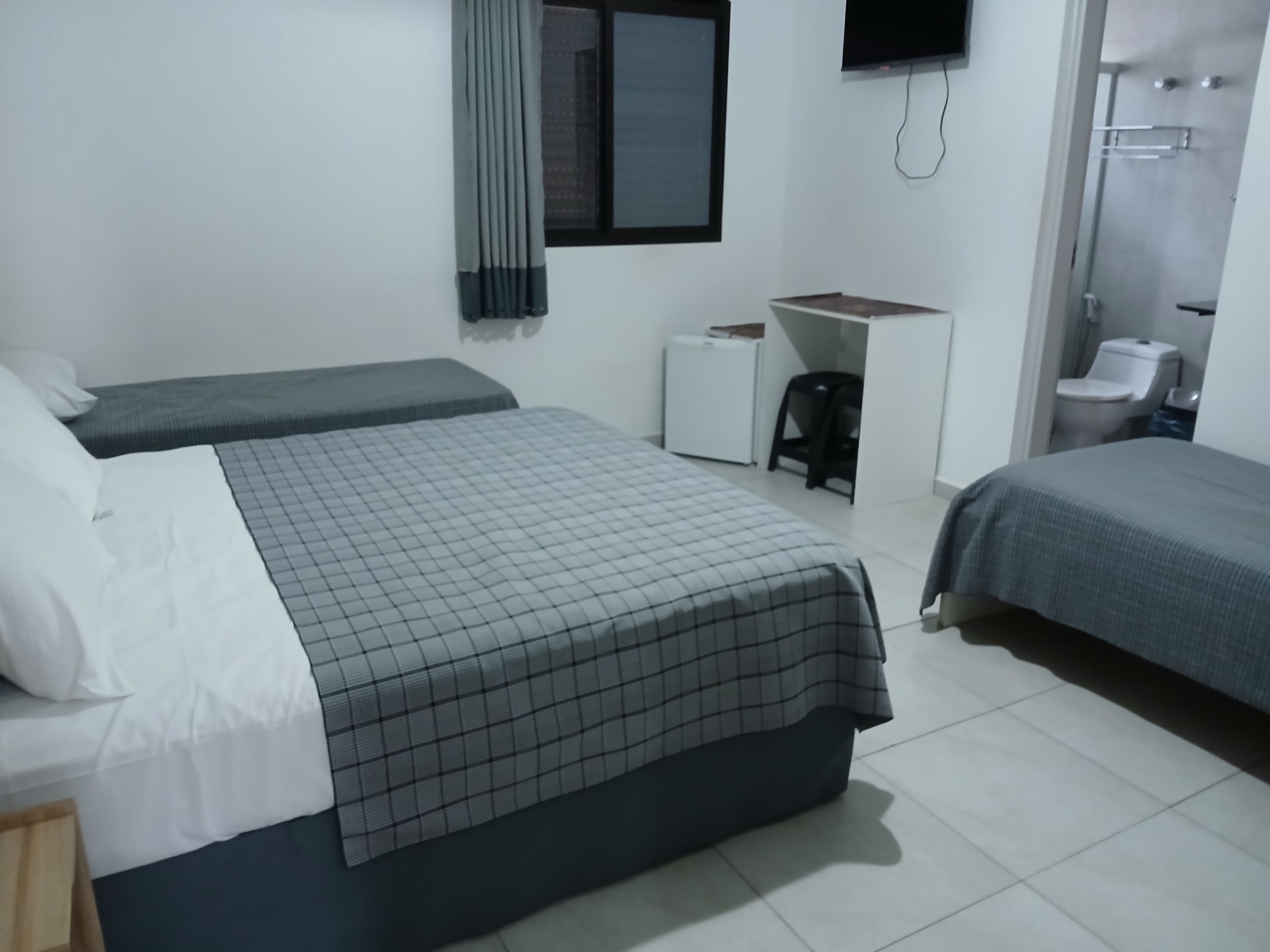 Ett hotellrum med två sängar, ett skrivbord, en stol, en toalett och en TV.