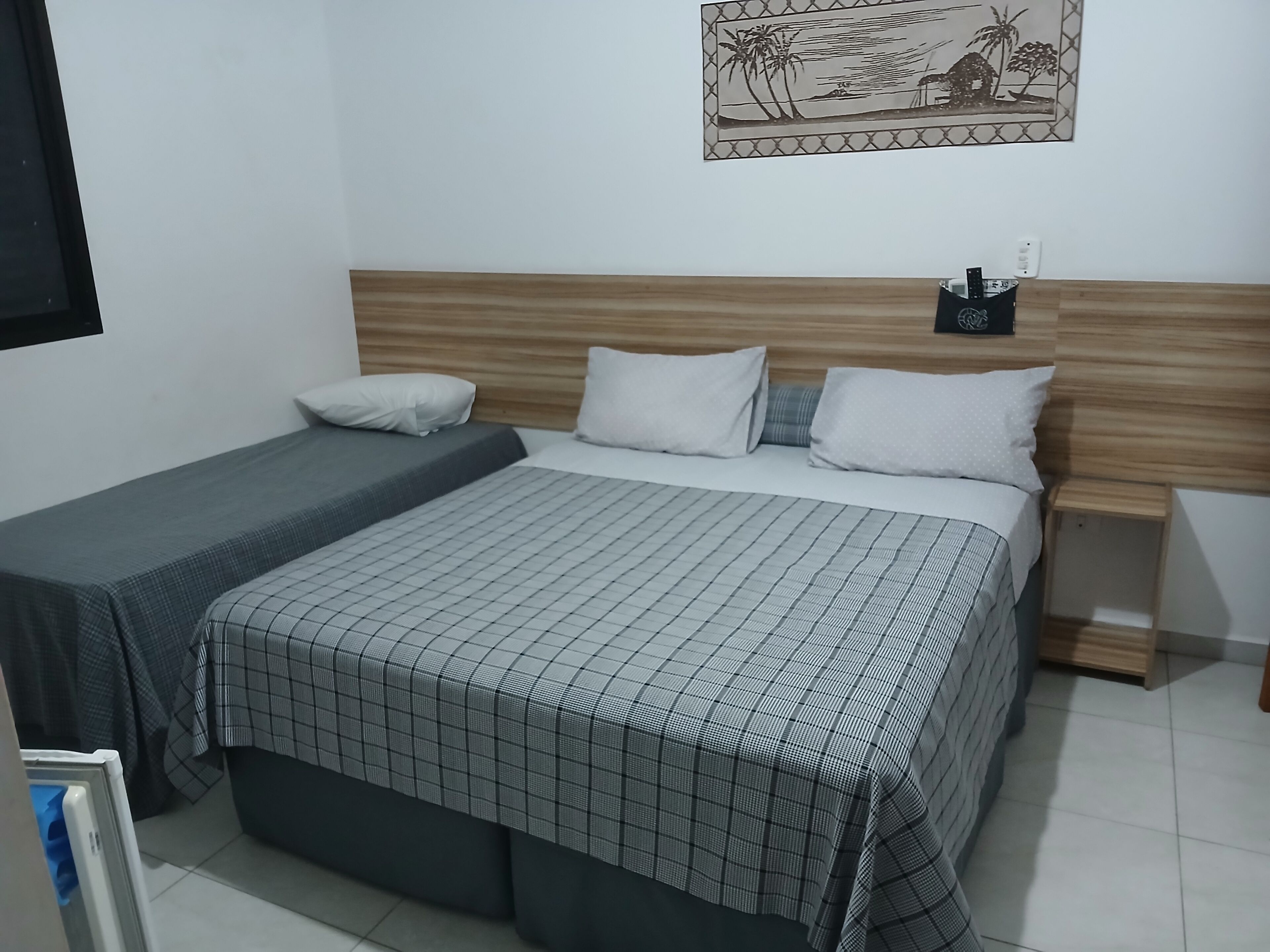 A bedroom with a large bed, a smaller bed, a nightstand, a wall-mounted phone, and a framed picture.