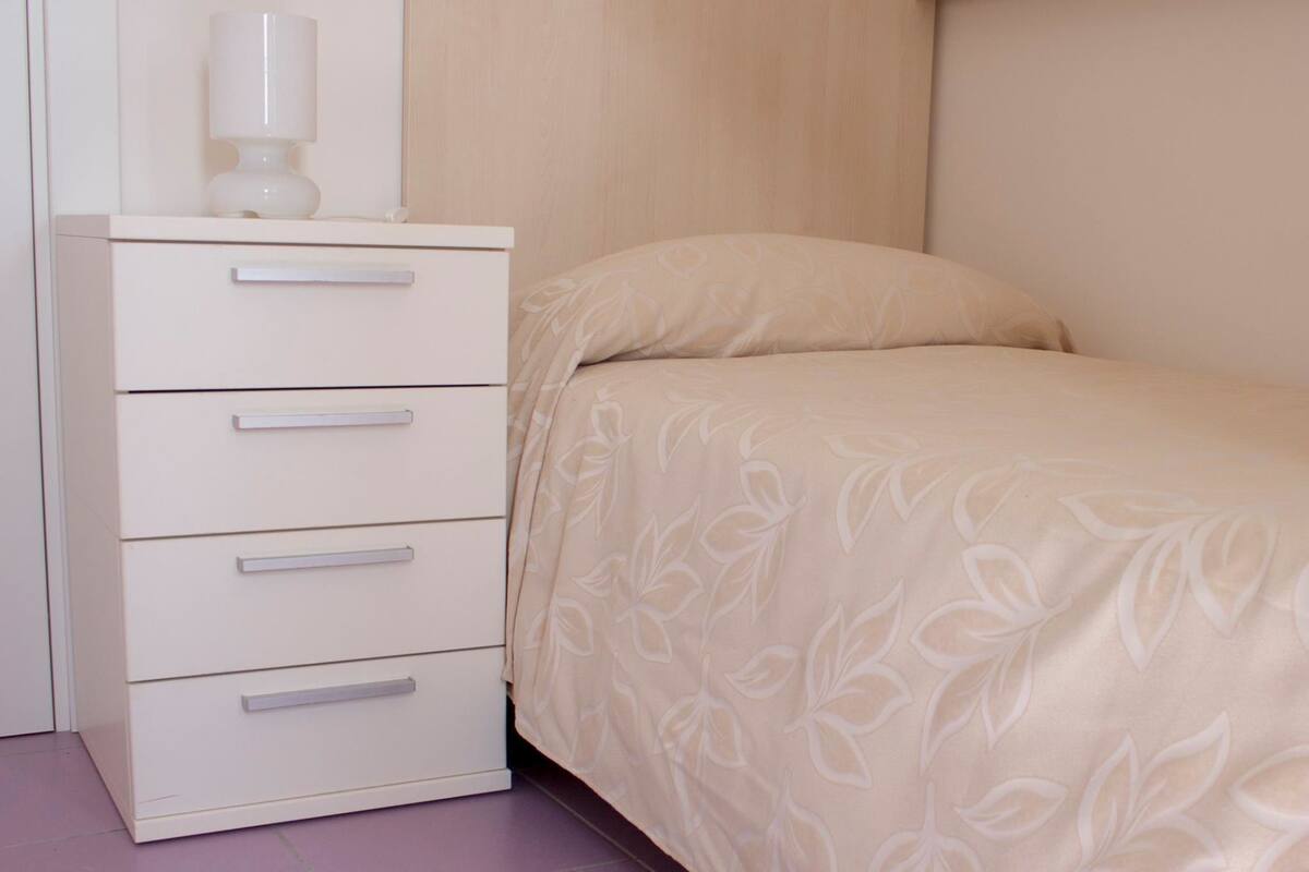 Une chambre à coucher avec un lit, une table de chevet avec une lampe et une commode avec des tiroirs.