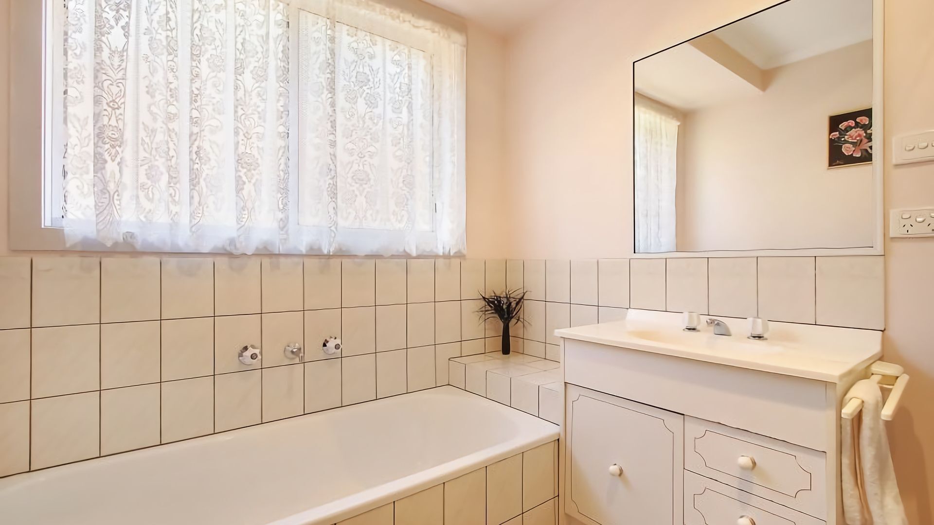 Een badkamer met een bad, een wastafel, een spiegel en een raam met kantgordijnen.