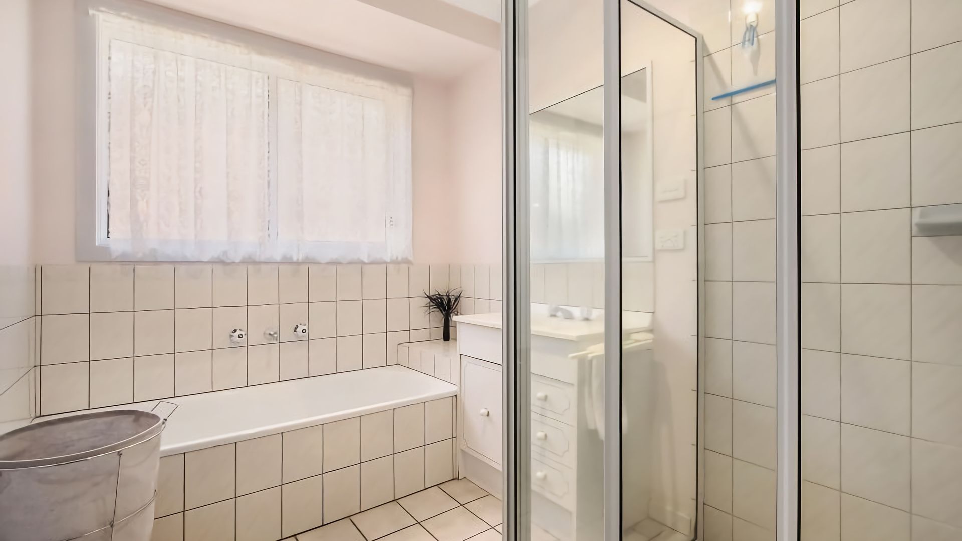 Une salle de bain moderne avec une douche à l’italienne en verre, une baignoire blanche et une fenêtre agrémentée d’un rideau blanc.
