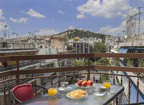 Un balcon avec une table dressée pour le petit-déjeuner, offrant une vue sur un paysage urbain avec des bâtiments et une colline.