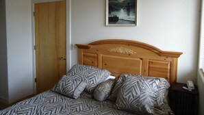 Ein Schlafzimmer mit einem hölzernen Kopfende, gemusterten Betttextilien, einem Bild an der Wand und einem Nachttischtelefon.