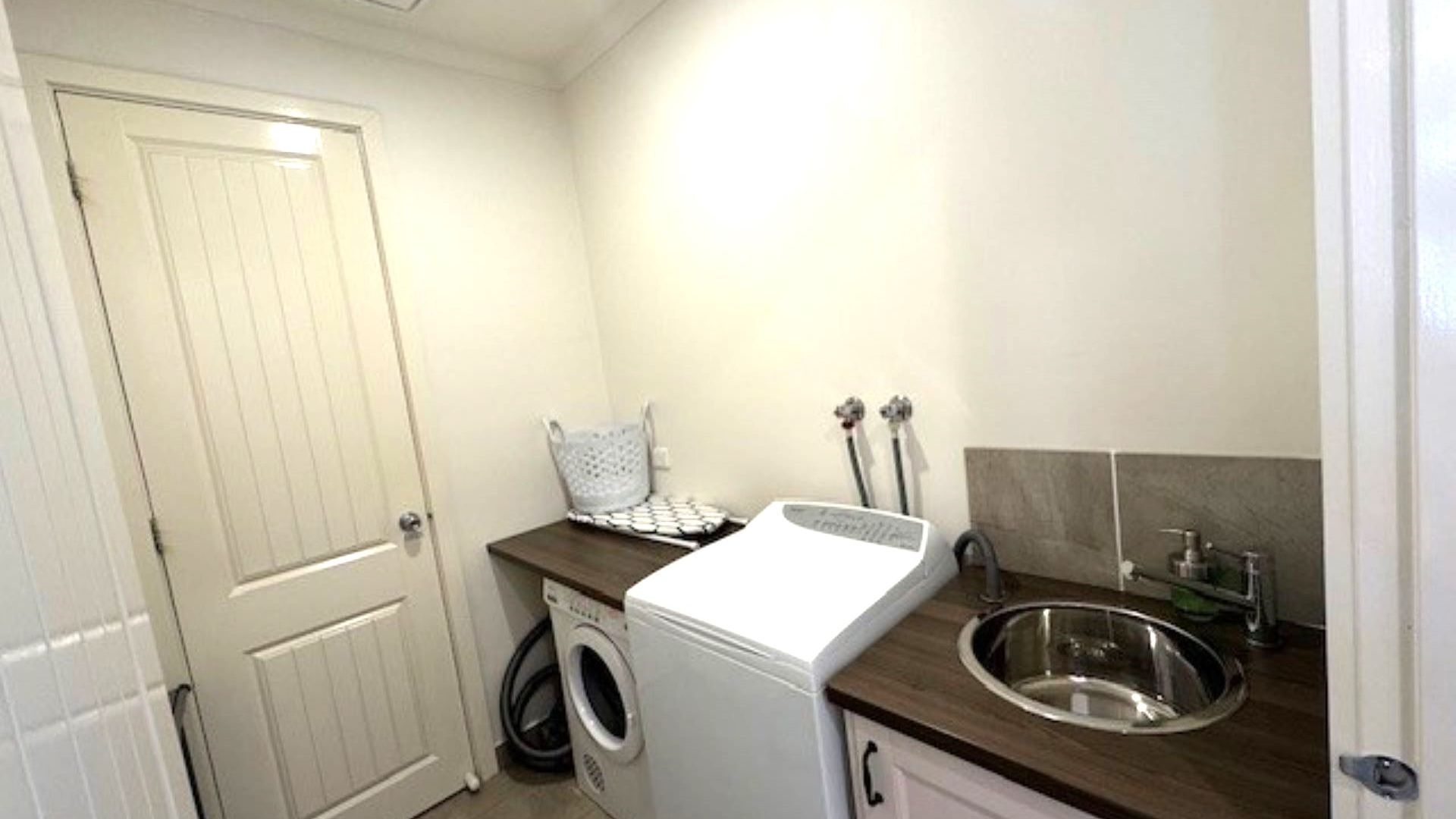 A compact laundry area with a washing machine, a sink, and a drying rack.