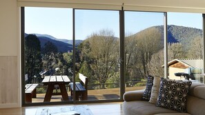 Quarto com uma grande porta de vidro deslizante que dá para uma varanda com mesa e cadeiras de piquenique, com vista para uma paisagem montanhosa.
