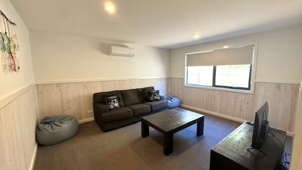 Uma sala de estar com sofá, mesa de centro, puff e televisão.