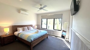 Una camera da letto con un letto, comodini, una ventola a soffitto, una finestra con persiane e una TV a parete.