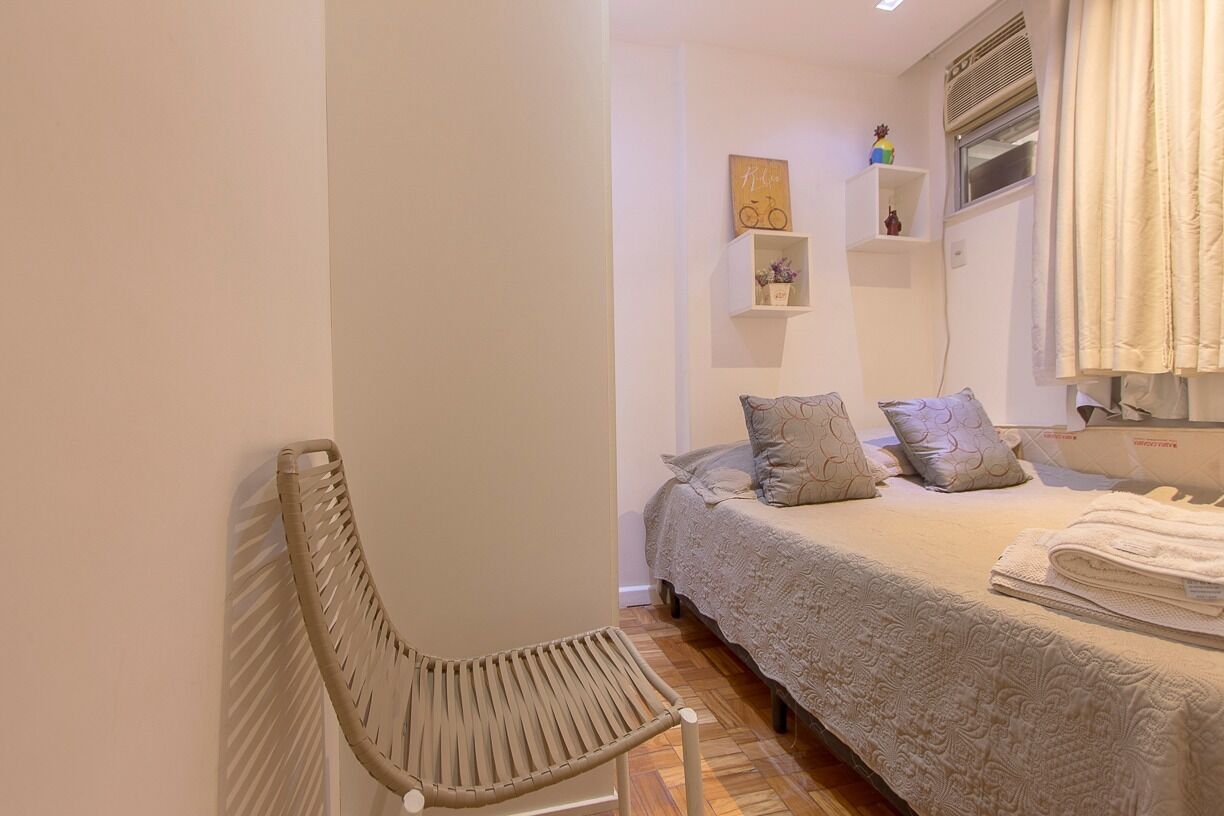A bedroom with a bed, a chair, a shelf with decorative items, and a window with curtains.