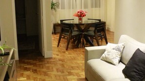 A living room with a wooden parquet floor, a white sofa with a black pillow, and a dining area with a table and chairs. - Make yourself at home in the best spot in Copacabana (the beach block)! (Rio de Janeiro)