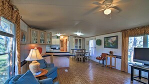 Ampla sala de estar com sofá, televisão, mesa de jantar e cozinha ao fundo.