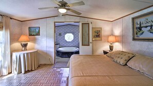 Quarto de hotel com cama, duas luminárias de cabeceira, ventoinha no teto, quadro na parede e banheiro visível através de uma porta aberta.