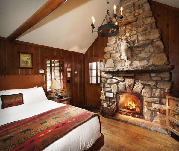 A cozy room with a stone fireplace, wooden walls, a large bed, and a nightstand with a lamp. - Big Cedar Lodge (Ridgedale)